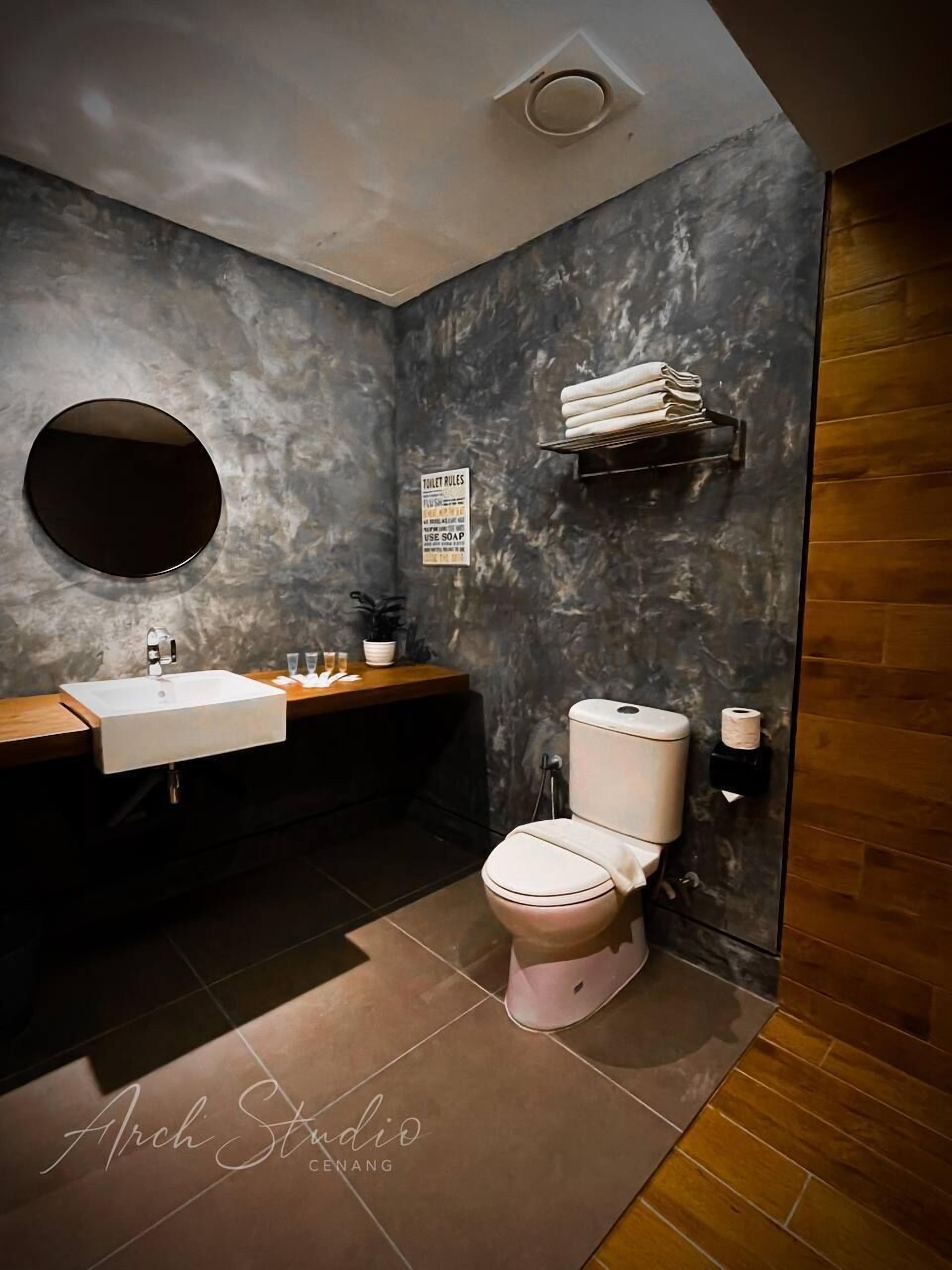 A modern bathroom with a marble wall, a round mirror, a sink, and a toilet.