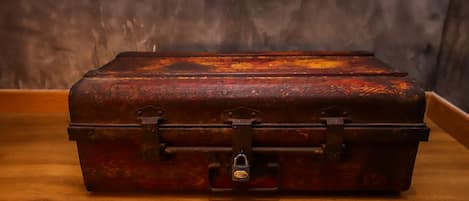 A vintage, metal suitcase with a lock on a wooden floor against a dark wall.