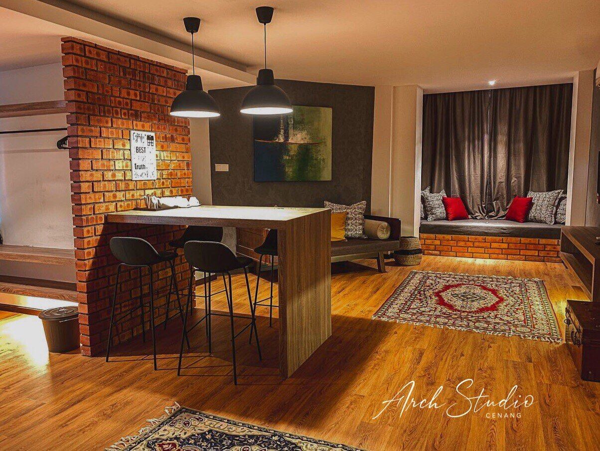 Una sala de estar moderna con una pared de ladrillo decorativa, una mesa de centro de madera, sillas negras, un sofá con cojines rojos y una alfombra grande.