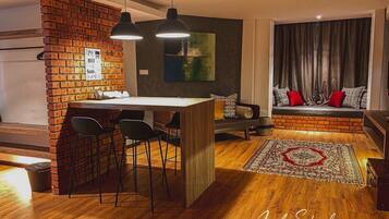 Una sala de estar moderna con una pared de ladrillo decorativa, una mesa de centro de madera, sillas negras, un sofá con cojines rojos y una alfombra grande.