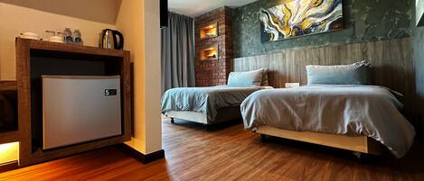 A hotel room with a bed, a small refrigerator, a brick accent wall, and a large abstract painting.