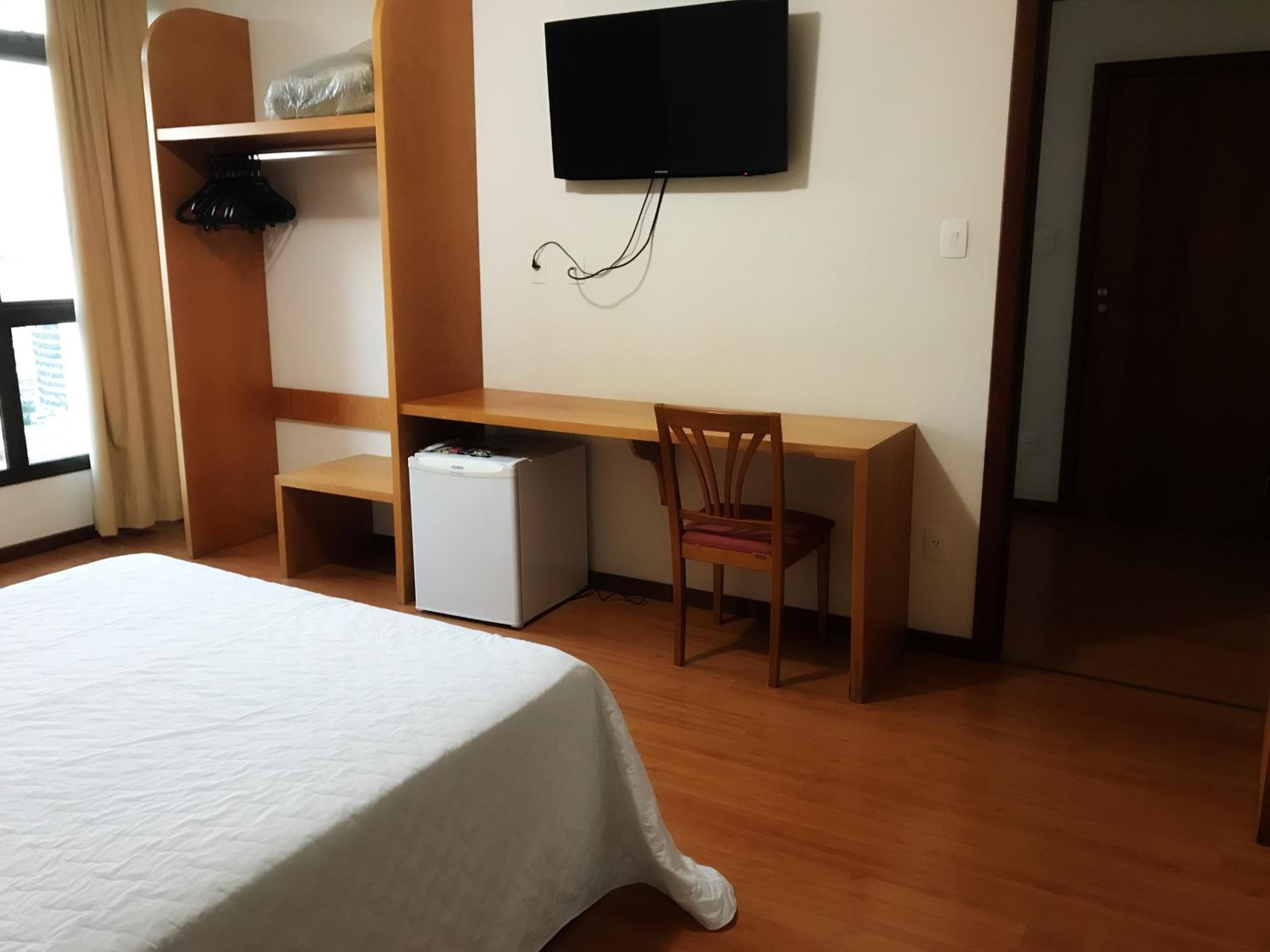 Ein Hotelzimmer mit Bett, Schreibtisch, Stuhl, Fernseher und kleinem Kühlschrank.