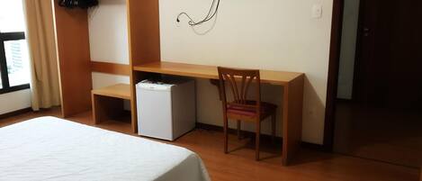 Ein Hotelzimmer mit Bett, Schreibtisch, Stuhl, Fernseher und kleinem Kühlschrank.