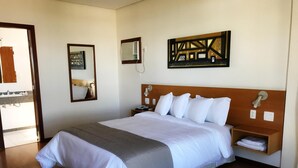 A hotel room with a large bed, a bedside table with a lamp, a wall-mounted air conditioner, and a framed picture. - Serema Palace Hotel (Lavras)