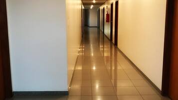 Un pasillo largo y bien iluminado con suelo de baldosas y puertas a ambos lados.