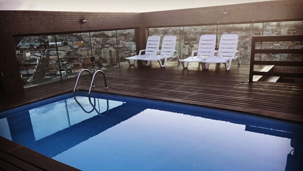 A rooftop swimming pool with wooden deck and white lounge chairs. - Serema Palace Hotel (Lavras)