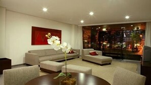 A modern living room with a sofa, ottoman, and a round table with a vase of flowers. - Serema Palace Hotel (Lavras)