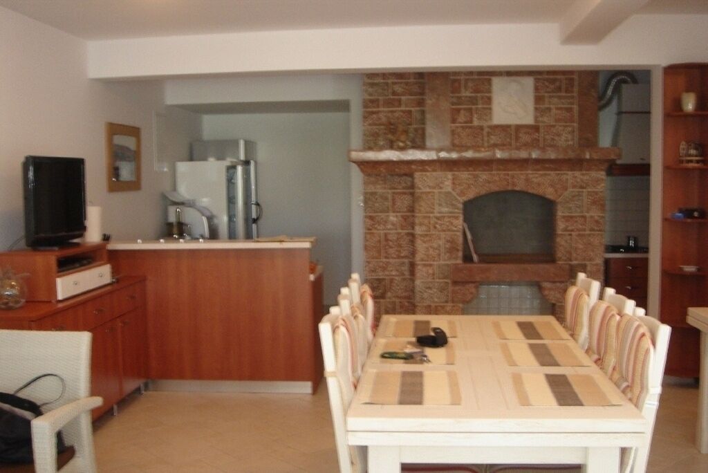 Un comedor con una mesa larga y sillas, una cocina con chimenea de ladrillo y un refrigerador.