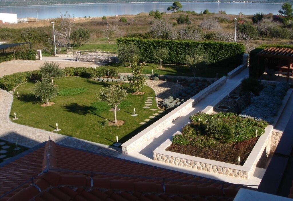 Um jardim paisagístico com caminhos, um pequeno lago e vista para um corpo d'água.