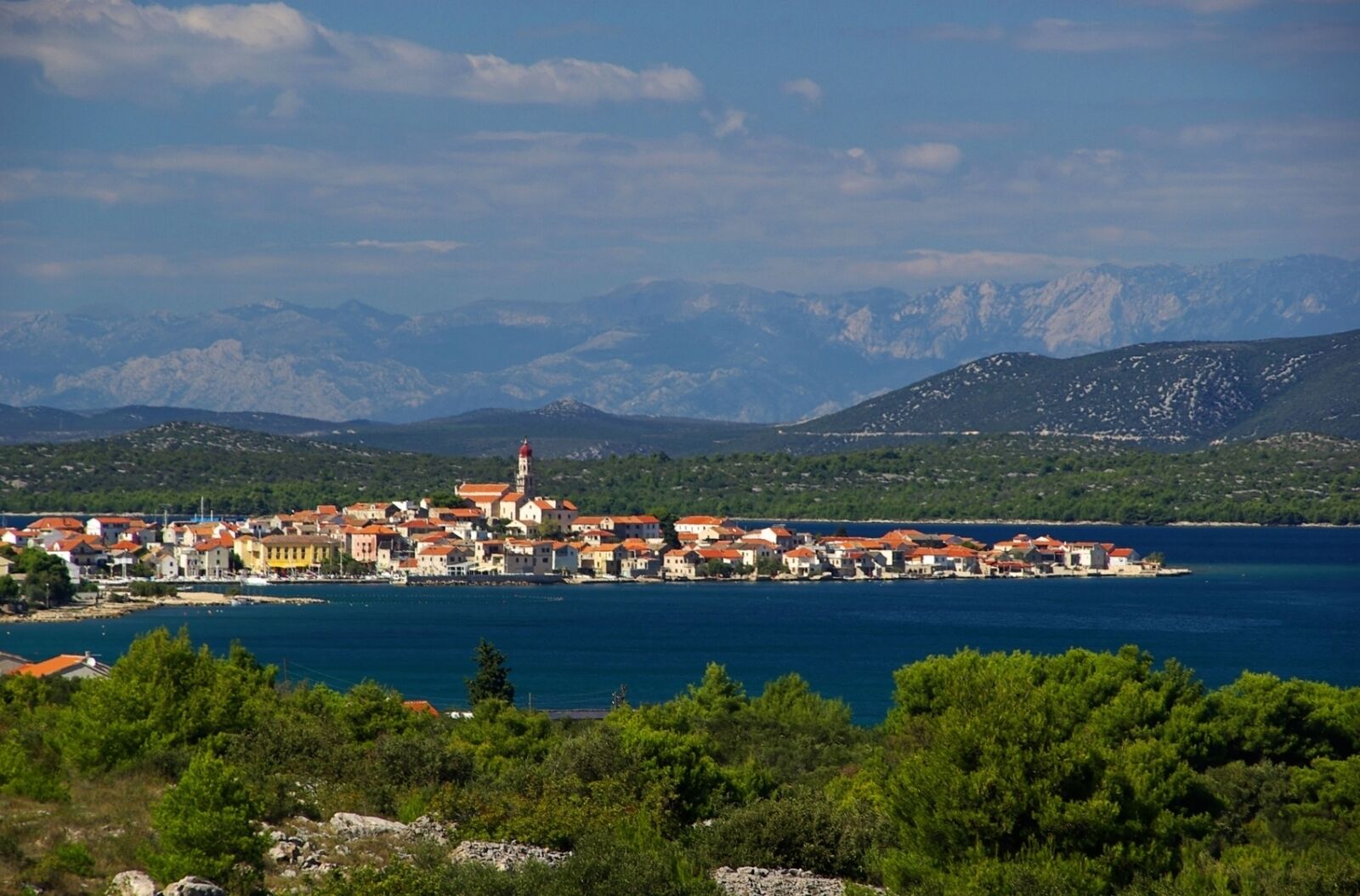Une ville côtière qui se distingue par son église imposante et offre une vue dégagée sur la mer et les montagnes en arrière-plan.