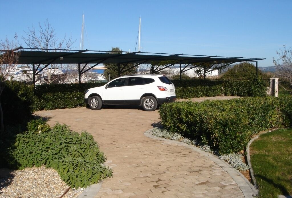 Un SUV blanco estacionado en un camino de entrada cubierto, con un sendero pavimentado que conduce a un edificio.