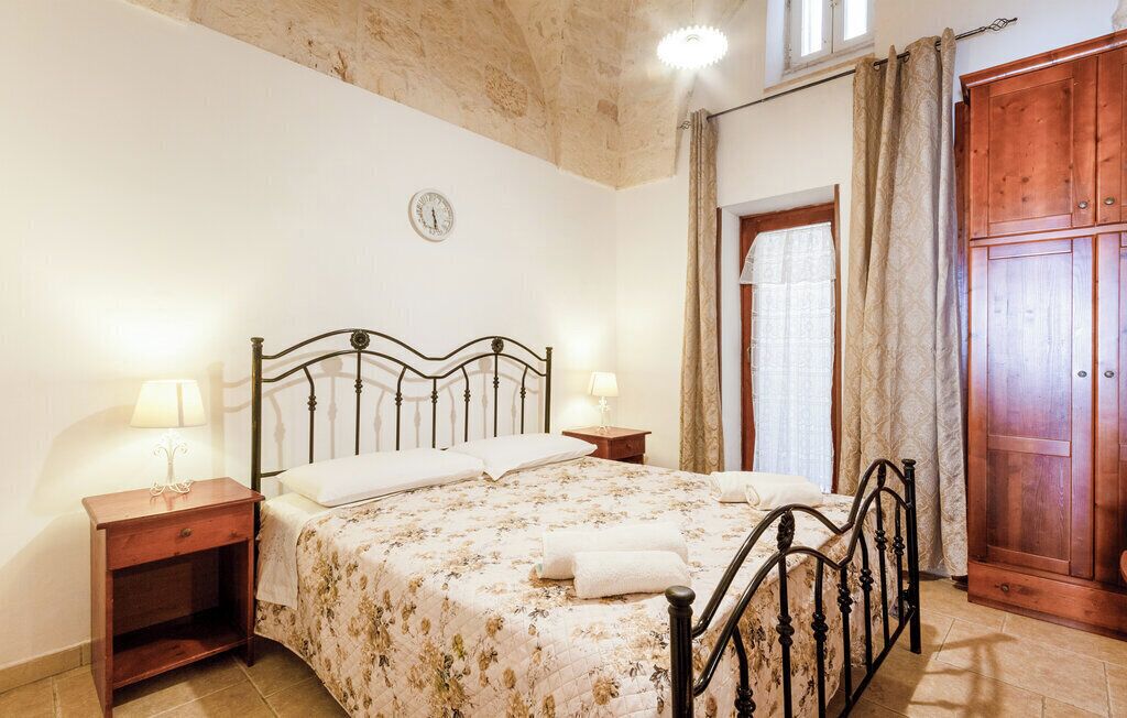 Een slaapkamer met een bed, twee nachtkastjes, een houten garderobe en een klok aan de muur.