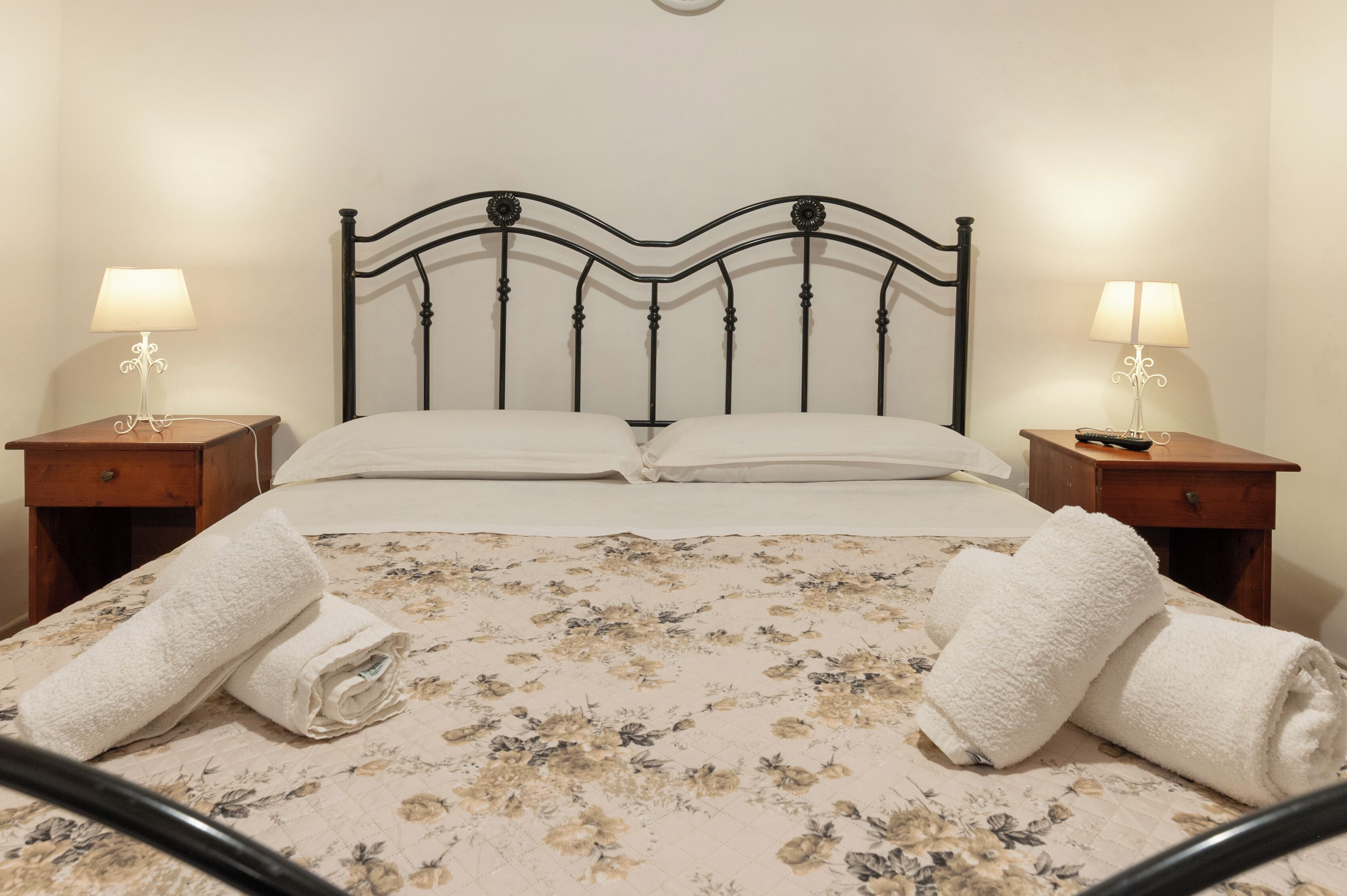 Un lit bien fait, avec une literie à motifs floraux, deux tables de chevet avec des lampes et des serviettes enroulées posées sur le lit.
