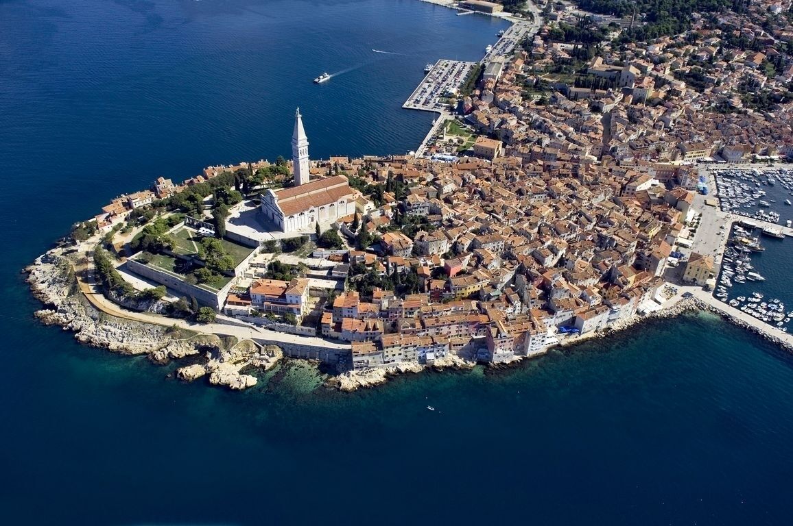 An aerial view of a coastal town with a prominent church, narrow streets, and a marina.