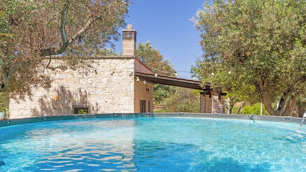 A swimming pool with a stone building in the background, surrounded by trees. - Casale Valle degli Ulivi (Ostuni)