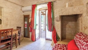 A room with a fireplace, a wooden table and chairs, and a bed with a patterned cover. - Casale Valle degli Ulivi (Ostuni)