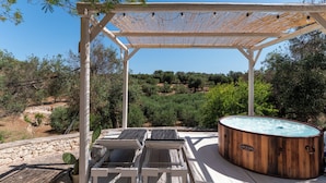 A wooden hot tub under a pergola with lounge chairs, surrounded by greenery and a stone wall. - Casale Valle degli Ulivi (Ostuni)