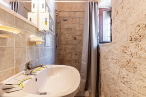 Un baño con un lavamanos blanco, ducha y ventana con vistas.