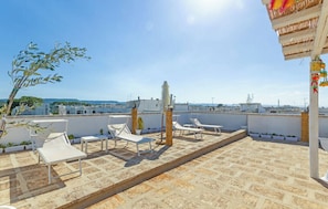 A rooftop terrace with white lounge chairs, a decorative column, and a view of the cityscape.
