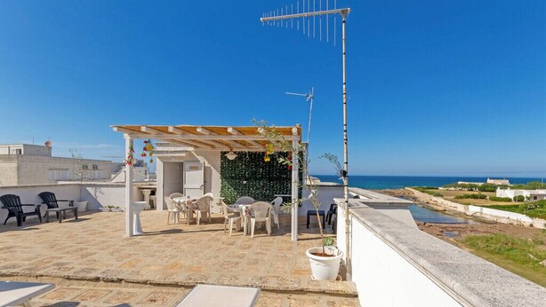 A rooftop terrace with outdoor seating, a pergola, and a view of the sea. - Appartamento La Rosa Dei Venti (Ostuni)