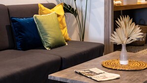 A modern living room with a sofa, cushions, a coffee table, a magazine, a plant, and a framed artwork on the wall. - Pame House (Athens)