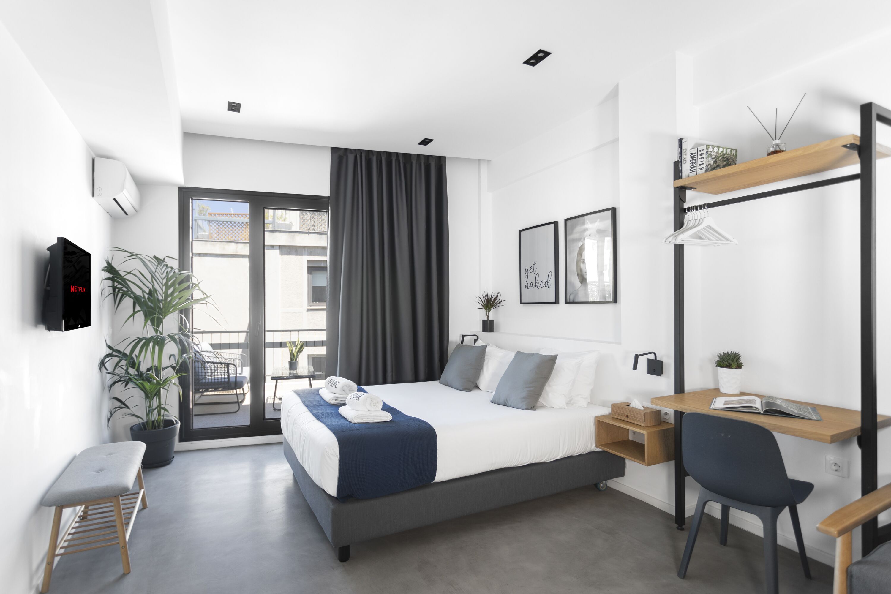 A modern hotel room with a large bed, a desk, a chair, a TV, and a balcony with a view.