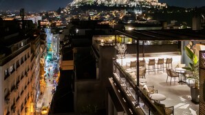 A rooftop terrace with outdoor seating, a view of a historic building, and a cityscape at night. - Pame House (Athens)