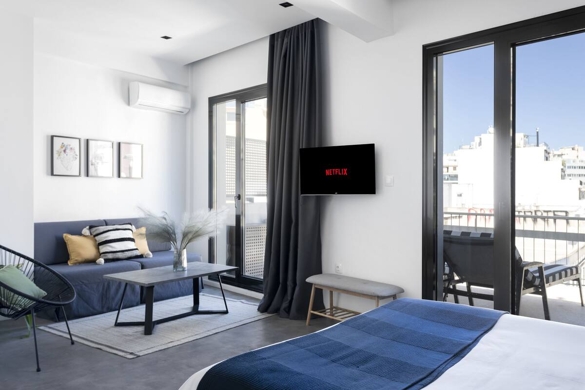 A modern hotel room with a large bed, a sofa, a small table, and a TV mounted on the wall.