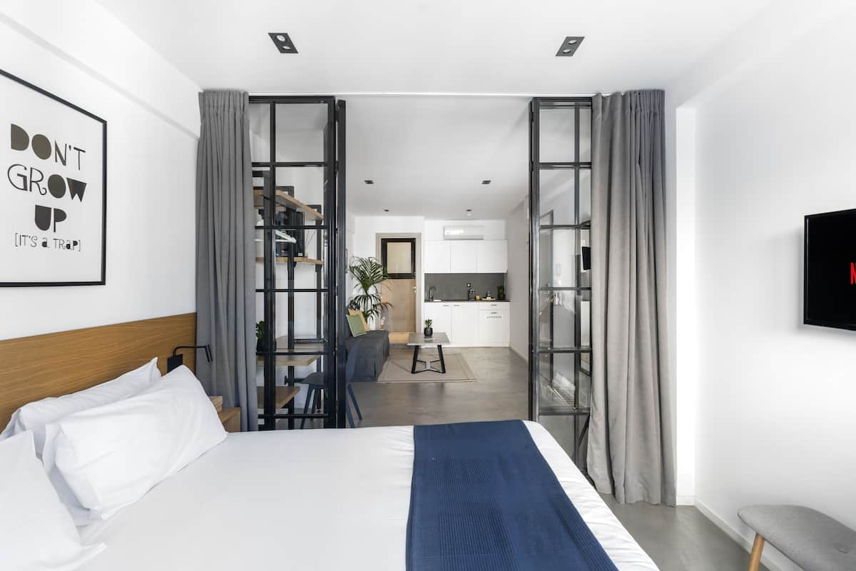 A modern hotel room with a large bed, a desk, and a kitchenette.