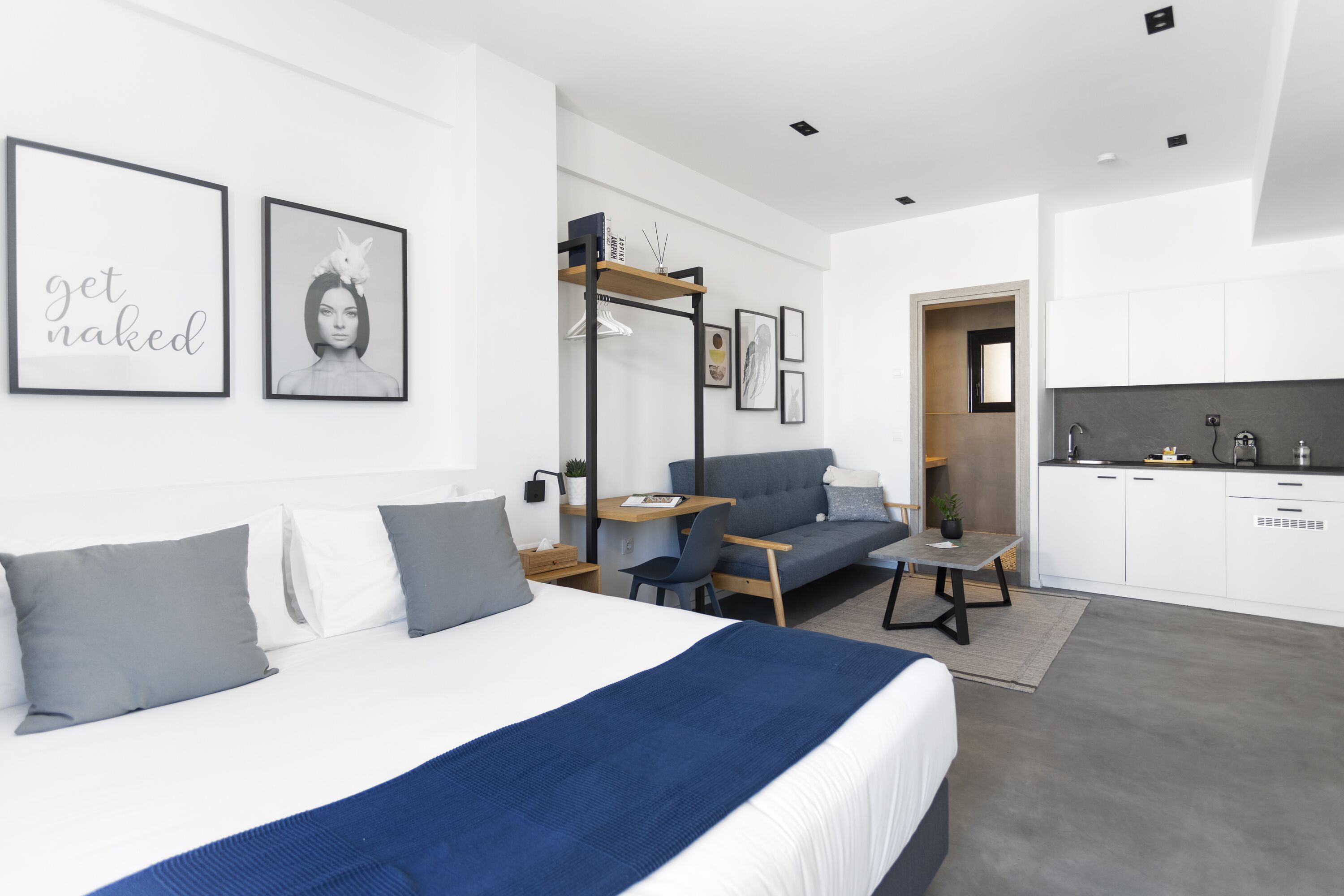 A modern hotel room with a bed, a desk, a sofa, and a kitchenette.