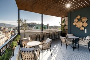 A rooftop terrace with wicker furniture, a view of the city, and a wall with circular wall art. - Pame House (Athens)