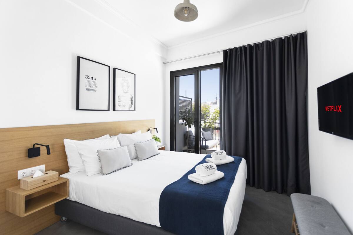 A modern hotel room with a large bed, a bedside table with a lamp, a TV, and a window with curtains.
