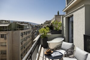 A balcony with a white bathtub, a potted plant, and a table with a hat and a book. - Pame House (Athens)