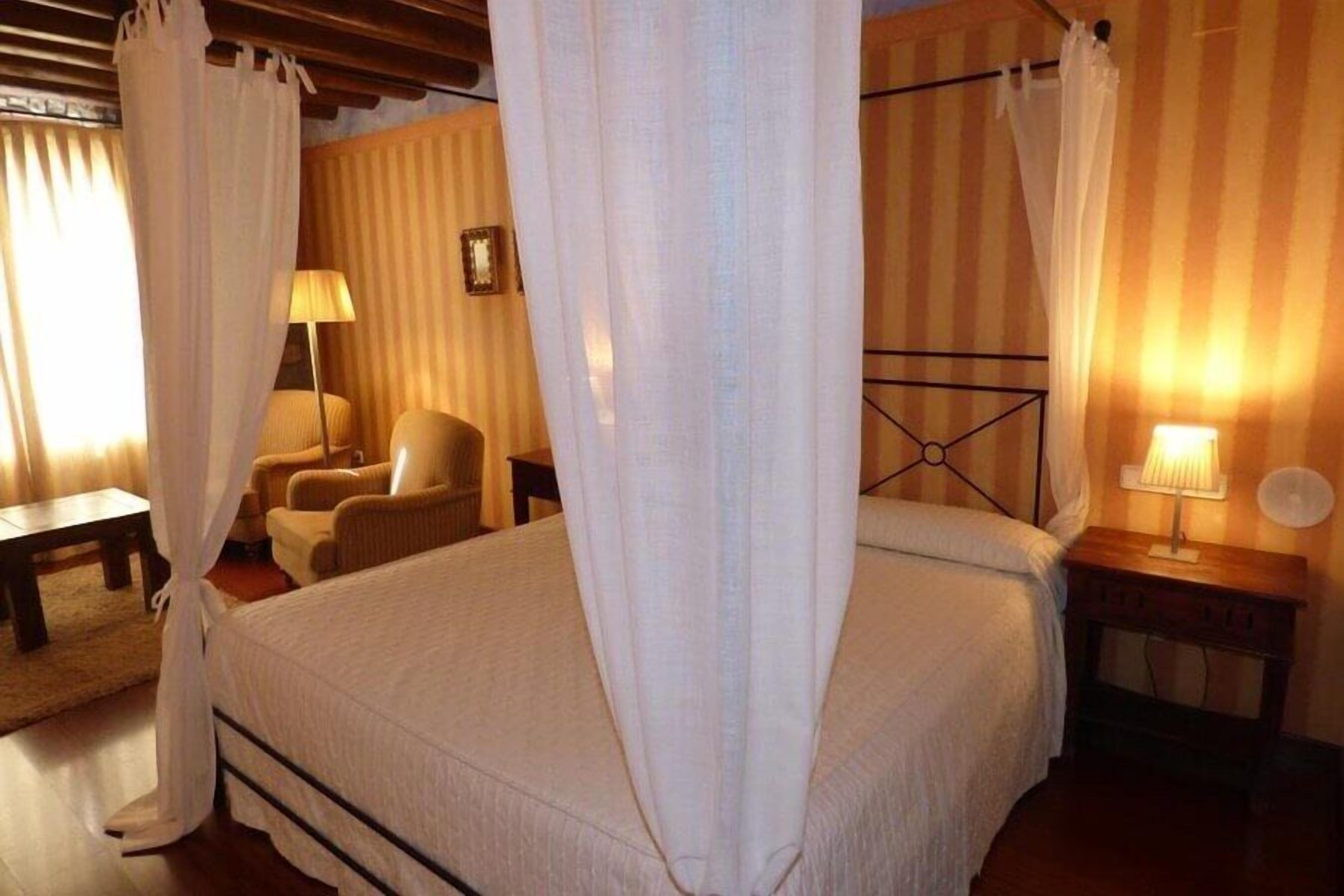 A bedroom with a bed, a chair, a bedside table, and a lamp.
