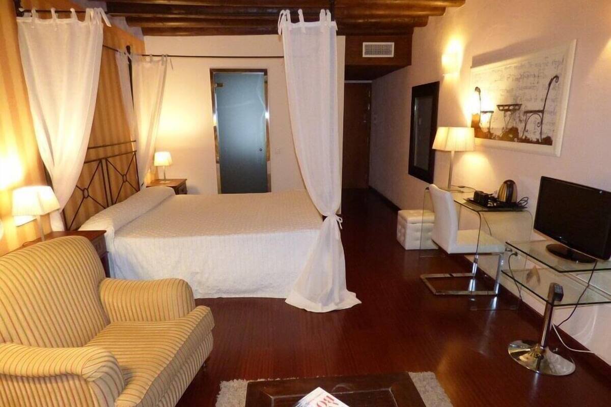 A hotel room with a bed, a chair, a desk with a computer, and a television.
