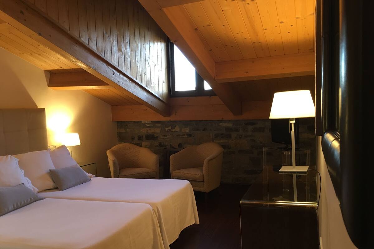 A cozy room with two beds, a stone wall, and a wooden ceiling.