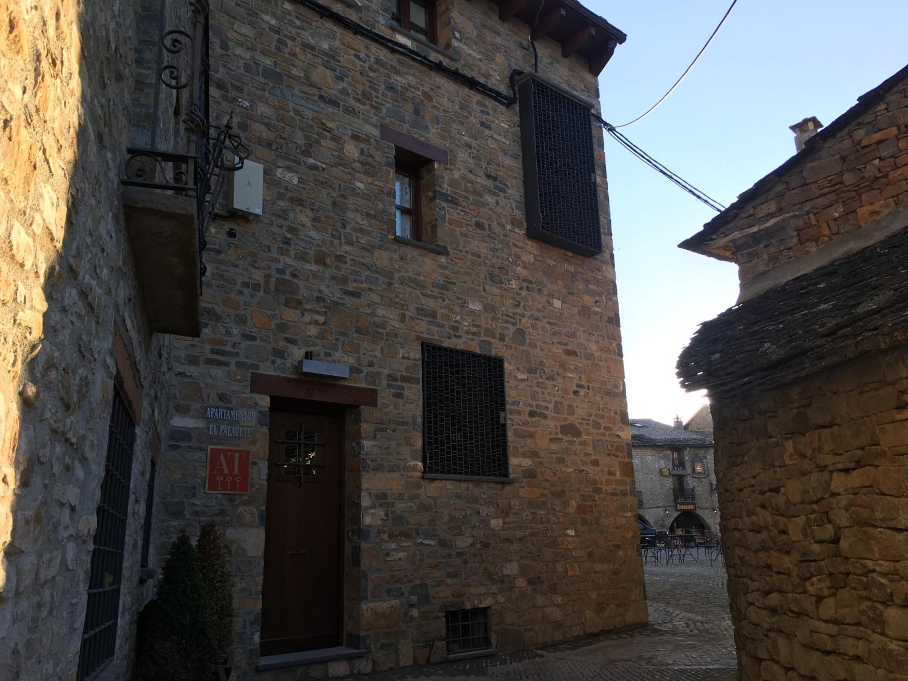 Un edificio de piedra con una puerta marrón, una ventana con celosía metálica y un letrero que indica que es un apartamento.