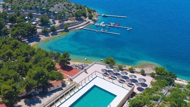 Vue aérienne d’une station balnéaire avec une piscine, une plage et des bateaux amarrés.