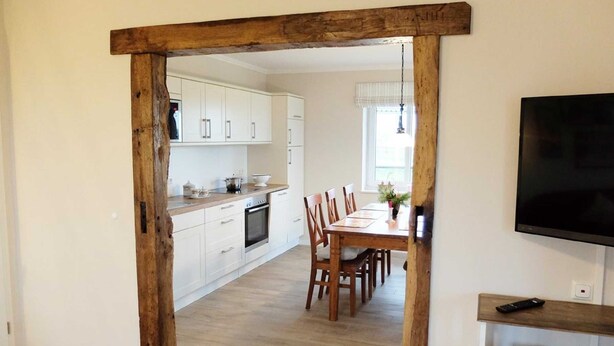 Une cuisine moderne avec des meubles blancs, une table à manger en bois et un téléviseur fixé au mur.