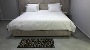 Une chambre avec une tête de lit en bois, un lit recouvert de linge de lit blanc et un tapis à motifs sur le sol.