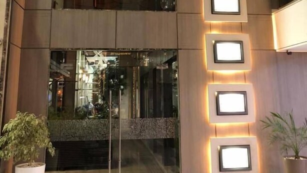 Une façade moderne avec une entrée en verre, des appliques murales illuminées et des plantes en pot.