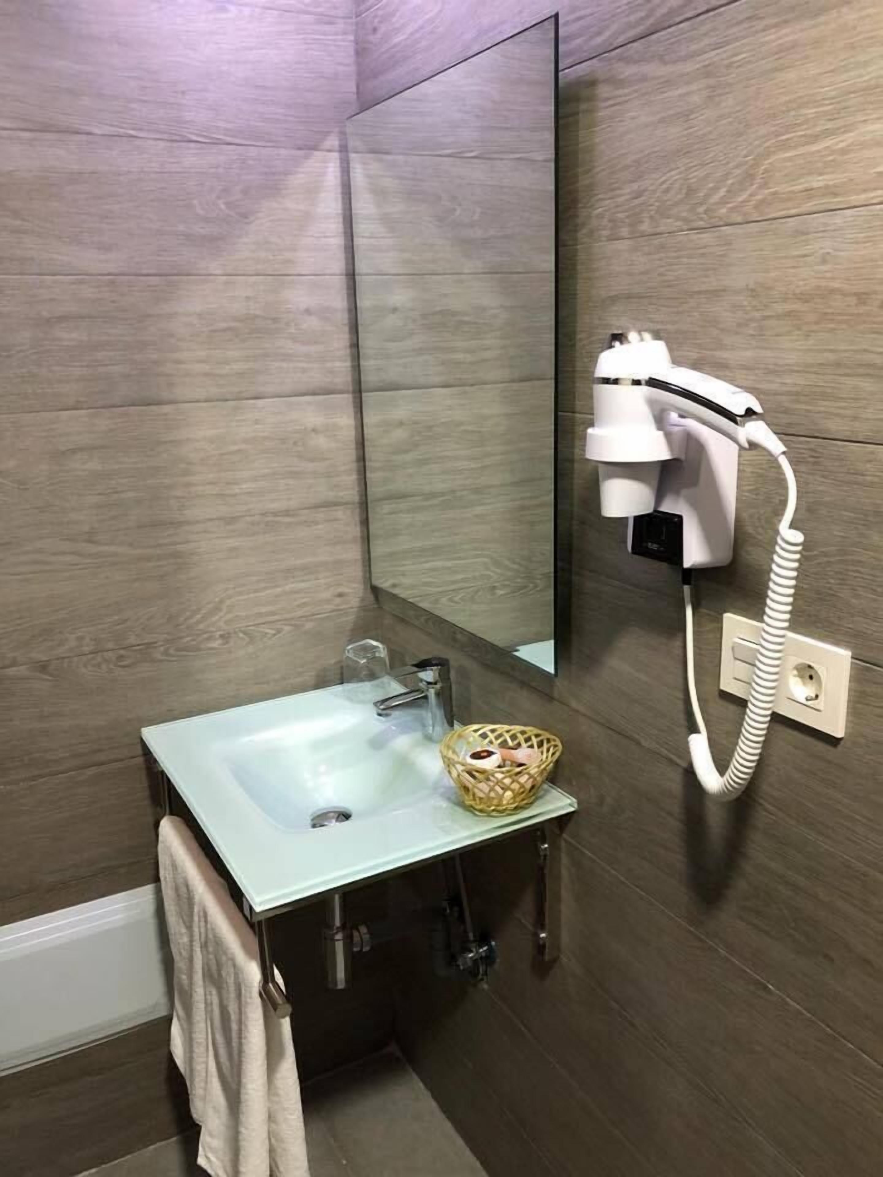 A bathroom with a sink, mirror, and hairdryer mounted on the wall.