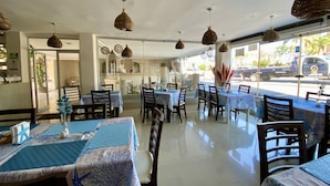 A restaurant interior with tables set for dining, hanging wicker lamps, and a view of the street outside. - Hotel Playa de Oro (Boca del Río)