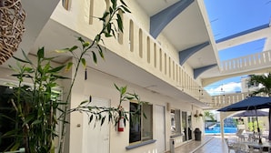 A covered outdoor area with tiled flooring, white metal chairs, and tables, a fire extinguisher, and a view of a swimming pool in the background. - Hotel Playa de Oro (Boca del Río)