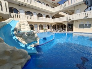 Una piscina con una formación rocosa y una zona cubierta con sillas.