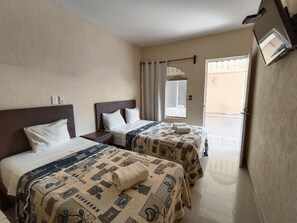 Habitación de hotel con dos camas, una ventana con cortinas, un televisor montado en la pared y una puerta que da al exterior.