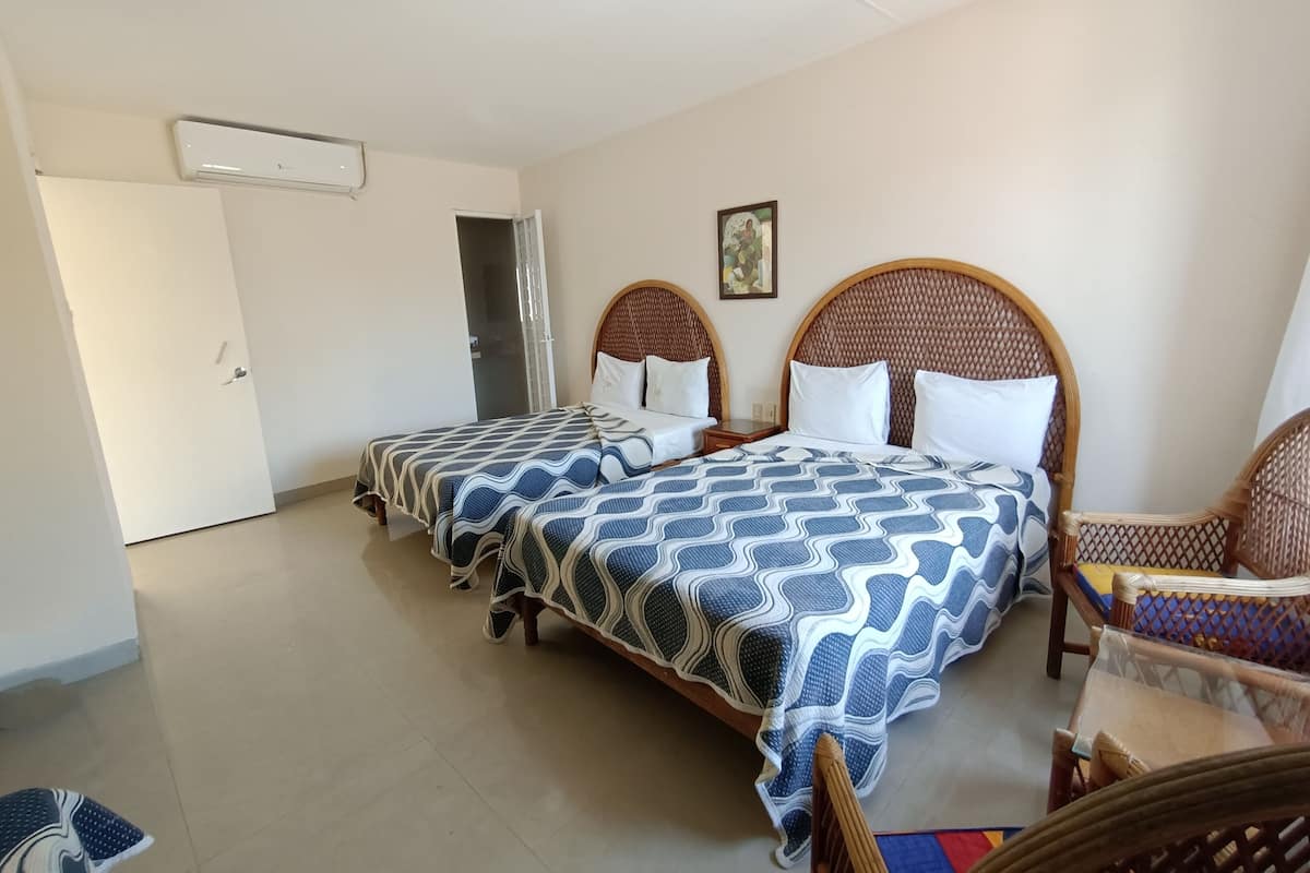 Habitación de hotel con dos camas individuales, un cabecero de madera, una puerta blanca y una mesita pequeña.