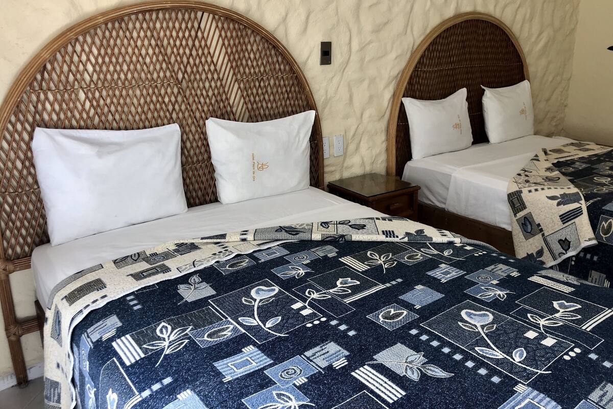 Dos camas individuales con cabeceros de mimbre, ropa de cama blanca y mantas estampadas.
