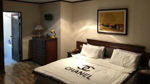 Ein Hotelzimmer mit einem Bett, das eine Chanel-Decke hat, einem Nachttisch mit Lampe, einem Bild an der Wand und einer hölzernen Kommode.