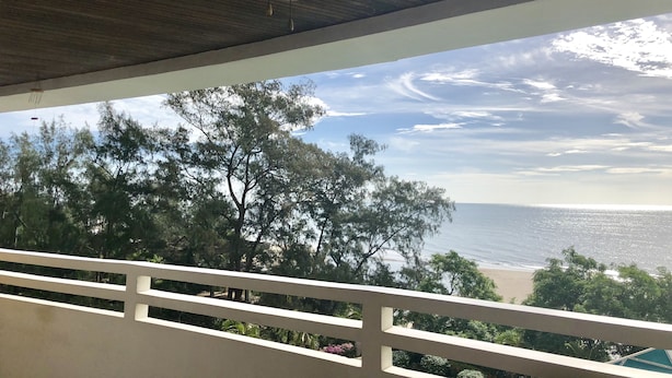 Ein Balkon mit Deckenventilator, mit Blick auf Strand und Bäume.